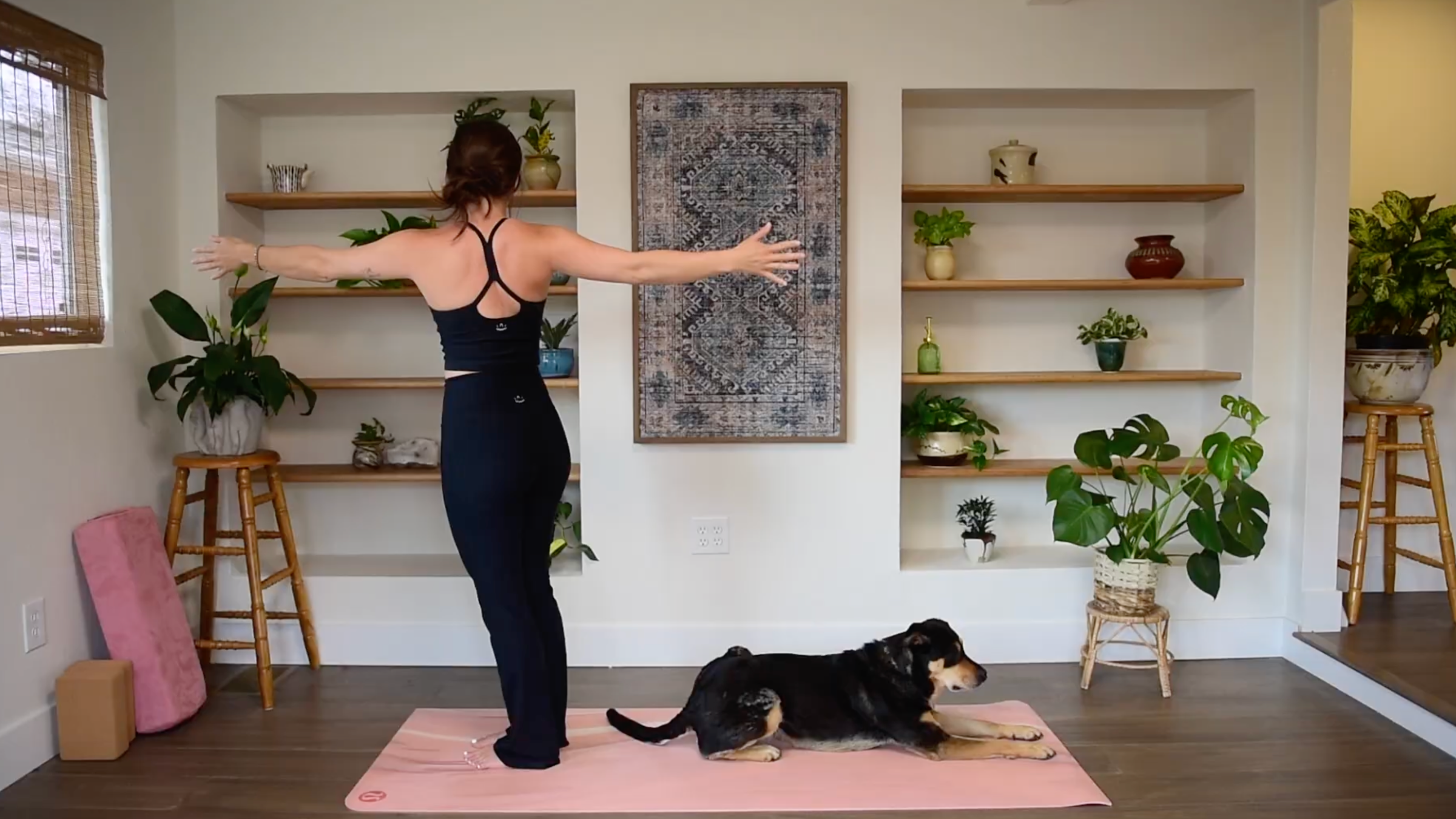 Caitlin K'eli standing on a yoga mat with arms extended in a T shape, twisting her torso toward the right side in a Standing Side Twist.